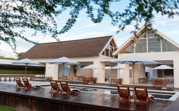 Zijaanzicht lodge met zwembad en ligstoelen op de voorgrond