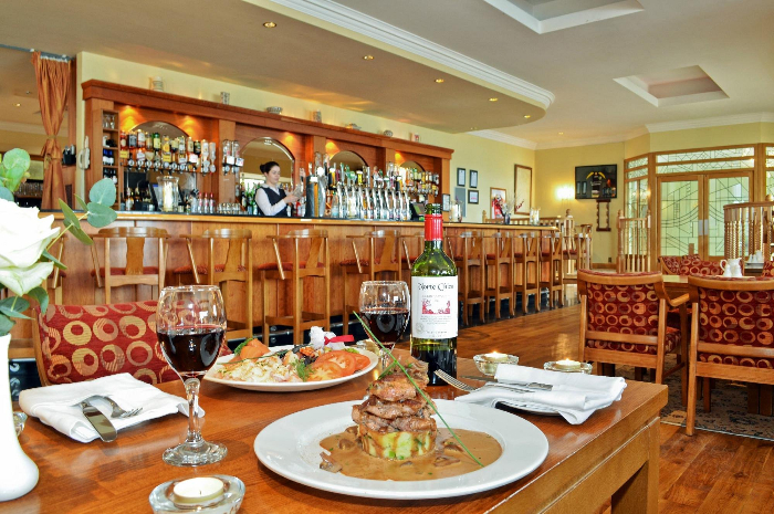 Houten bar in het Broadhaven Bay Hotel, met 2 borden met eten en 2 glazen wijn op de voorgrond