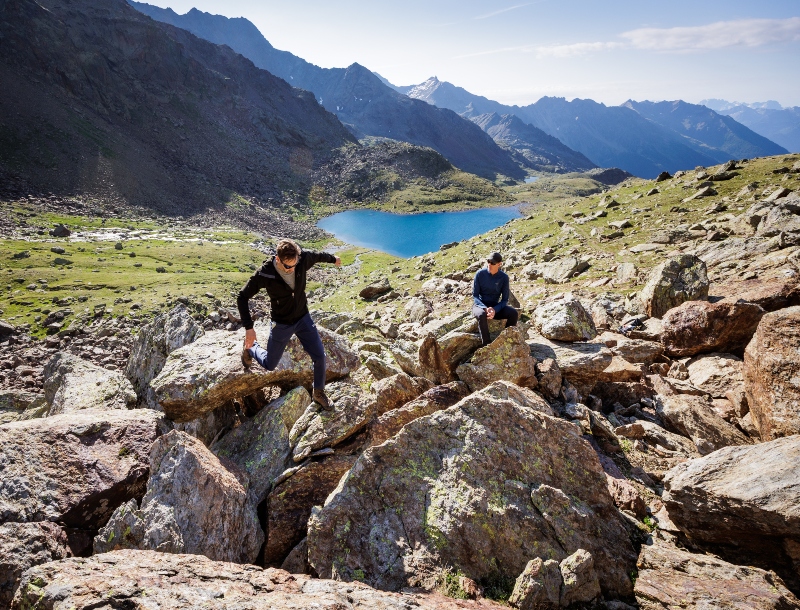 Evenwichtsoefeningen op rotsblokken in de Alpen, met Lago Marmotta op de achtergrond